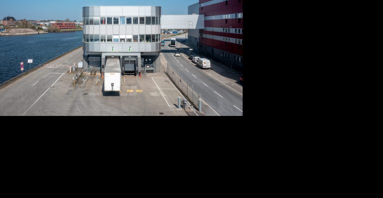 Luftaufnahme des modernen Büro- und Logistikgebäudes von H. & J. Brüggen KG an der Hafenstraße 5 mit einem LKW am Ladedock und einem Fluss im Hintergrund.