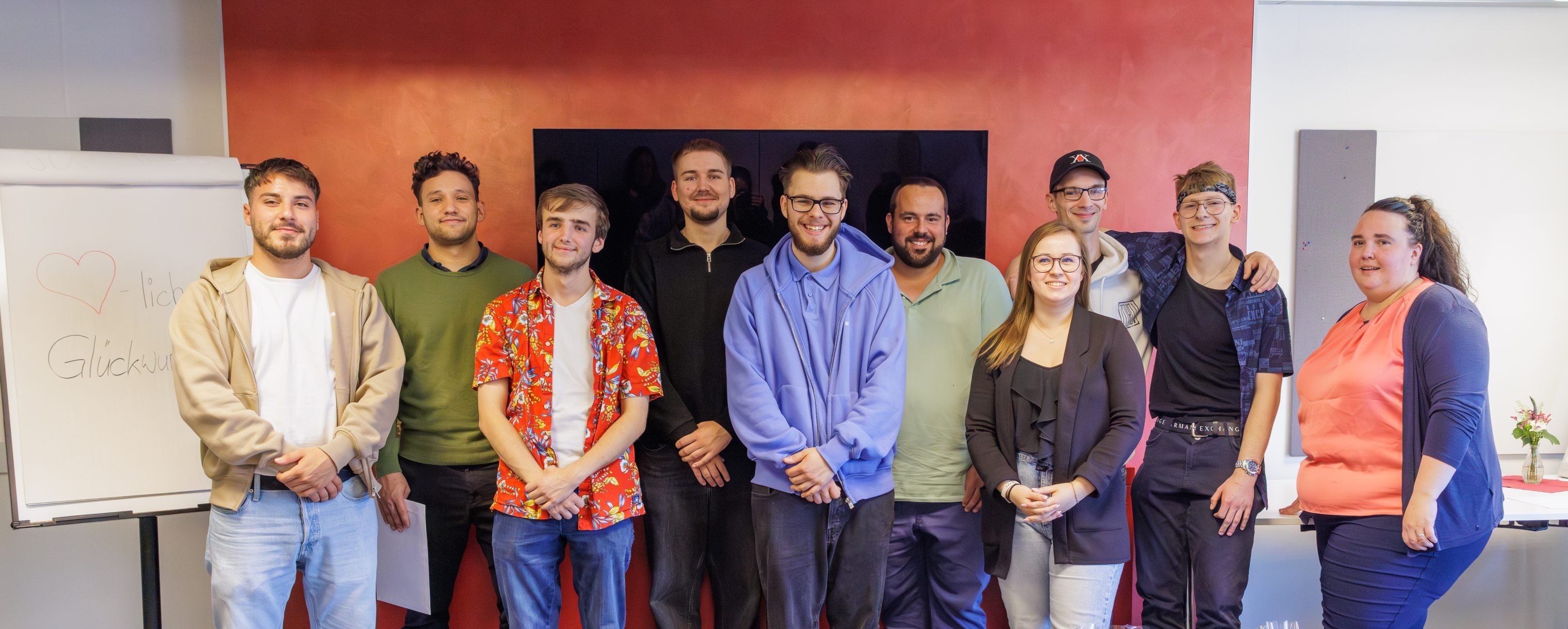 Zehn Auszubildende stehen in zwei Reihen und lächeln für ein Gruppenfoto in die Kamera.